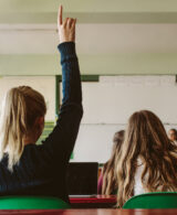 An image of a girl in a classroom raising her hand
