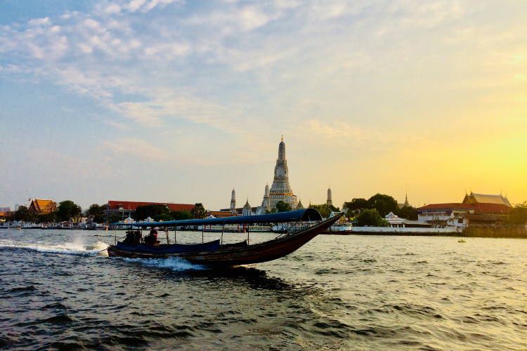 An image of a boat travelling on the Phraya River in front of the Wat Arun Temple