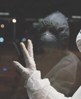 An image of a person in a Hazmat suit looking out the window at night